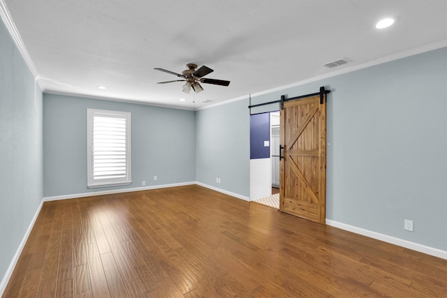 spare room featuring hardwood / wood-style flooring, ornamental molding, a barn door, and ceiling fan