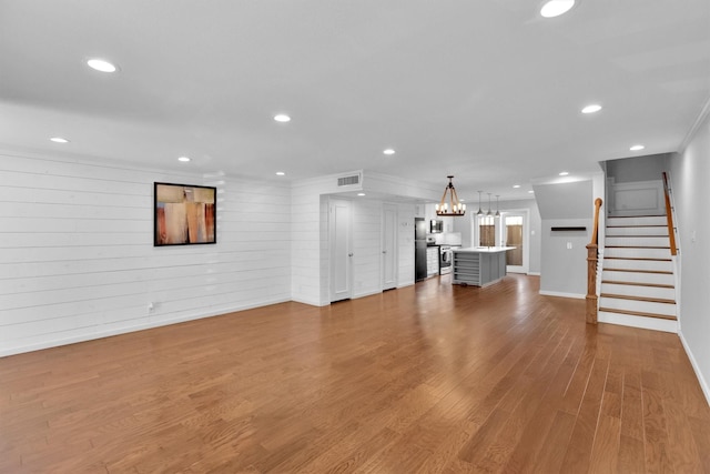 unfurnished living room with light hardwood / wood-style flooring, wooden walls, ornamental molding, and an inviting chandelier