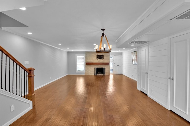 unfurnished living room with hardwood / wood-style flooring, wood walls, ornamental molding, and a notable chandelier