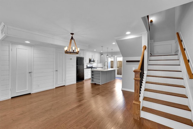 interior space featuring black refrigerator, pendant lighting, sink, white cabinets, and a center island with sink