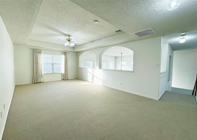 unfurnished room with a tray ceiling, ceiling fan, carpet flooring, and a textured ceiling