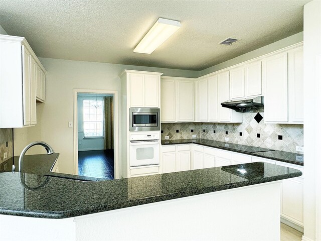 kitchen with stainless steel microwave, white oven, decorative backsplash, black electric stovetop, and white cabinets