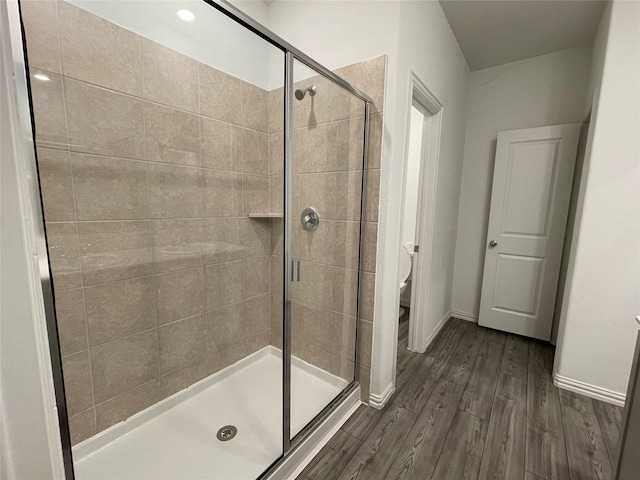 bathroom with a shower with shower door, hardwood / wood-style floors, and toilet