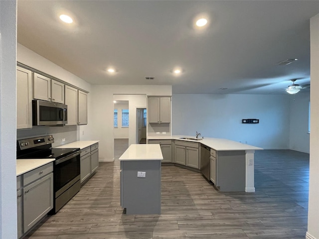 kitchen with sink, gray cabinets, appliances with stainless steel finishes, a center island, and kitchen peninsula