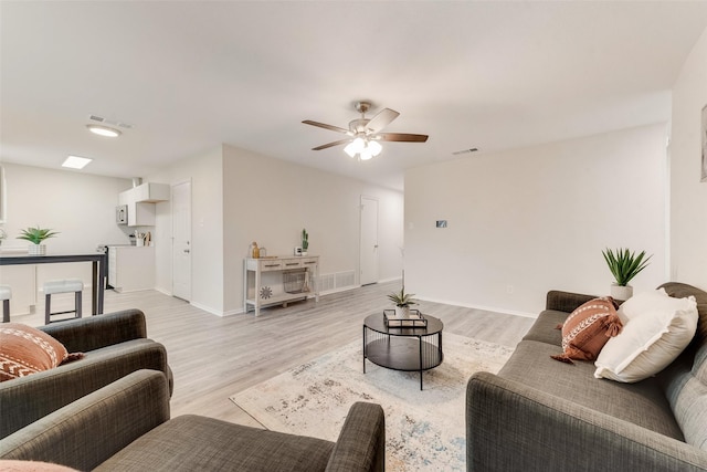 living room with ceiling fan, baseboards, visible vents, and light wood-style floors