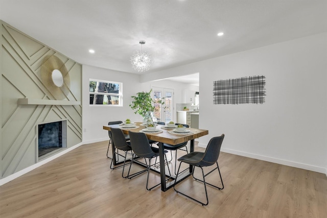 dining room with a large fireplace, a notable chandelier, and light wood-type flooring