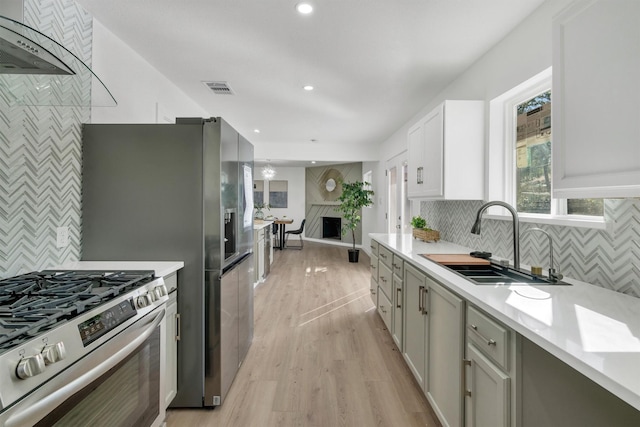 kitchen with a large fireplace, stainless steel gas stove, sink, backsplash, and light wood-type flooring