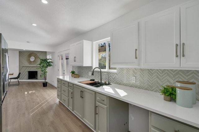 kitchen featuring tasteful backsplash, sink, light hardwood / wood-style flooring, a fireplace, and white cabinetry