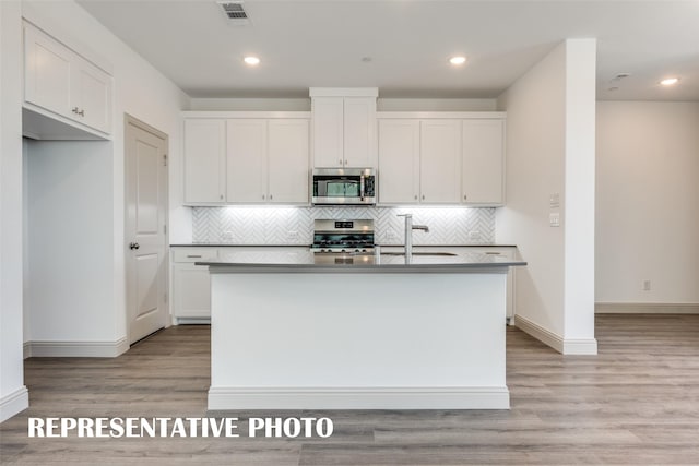 kitchen featuring white cabinets, light wood-type flooring, stainless steel appliances, and an island with sink