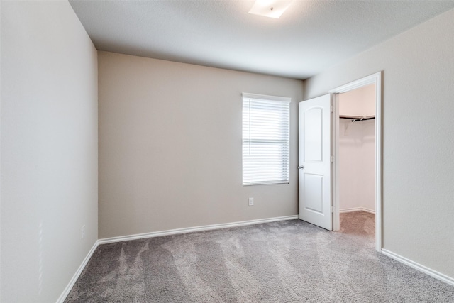 unfurnished bedroom featuring carpet flooring, a walk in closet, and a closet