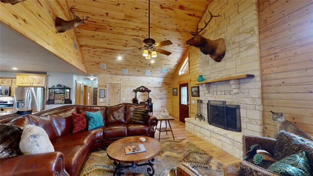 living room featuring high vaulted ceiling, a stone fireplace, wooden walls, and light hardwood / wood-style flooring