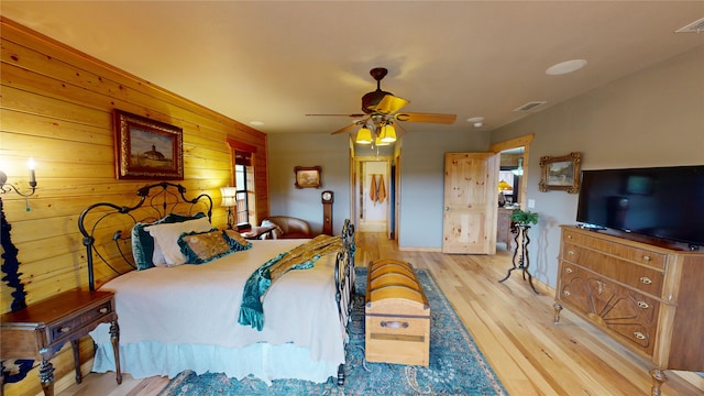 bedroom featuring ceiling fan, wood walls, and light hardwood / wood-style floors