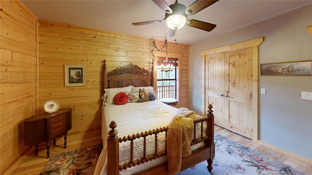 bedroom with hardwood / wood-style floors, ceiling fan with notable chandelier, and wood walls