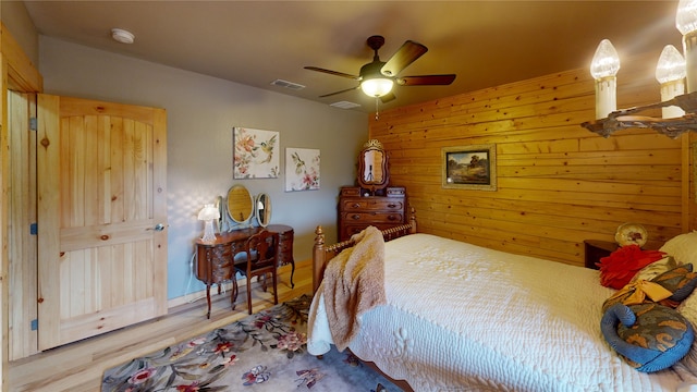 bedroom with ceiling fan, wood walls, and light wood-type flooring