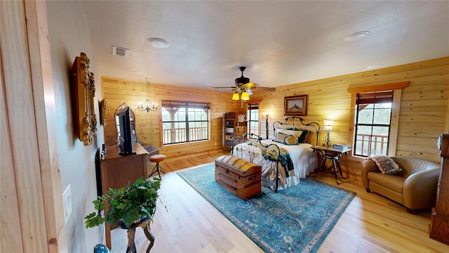 bedroom featuring ceiling fan with notable chandelier, wood walls, and wood-type flooring