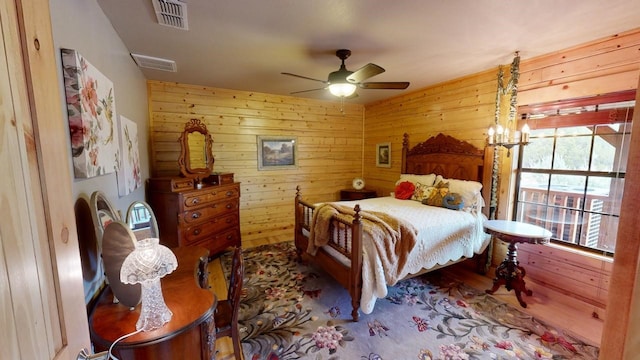 bedroom with wooden walls and ceiling fan with notable chandelier