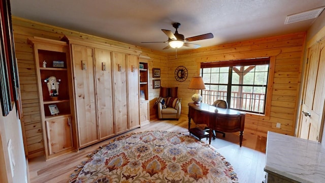 home office featuring ceiling fan, wooden walls, and light hardwood / wood-style flooring