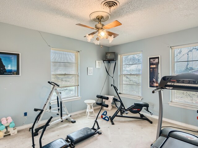 exercise area with a wealth of natural light, a textured ceiling, light colored carpet, and ceiling fan