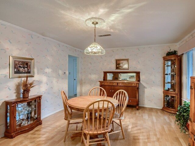 dining room with light hardwood / wood-style floors, ornamental molding, and an inviting chandelier