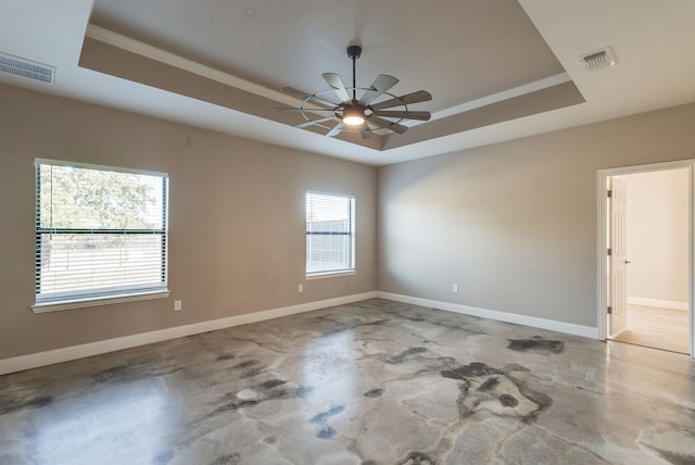 empty room with a raised ceiling, ceiling fan, and concrete floors