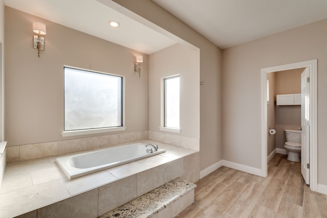 bathroom with wood-type flooring, tiled bath, and toilet