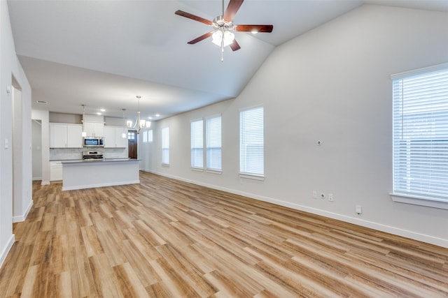 unfurnished living room with ceiling fan with notable chandelier, vaulted ceiling, and light hardwood / wood-style floors