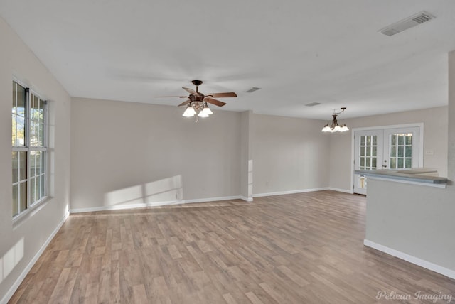 empty room featuring ceiling fan with notable chandelier, light wood-type flooring, and french doors