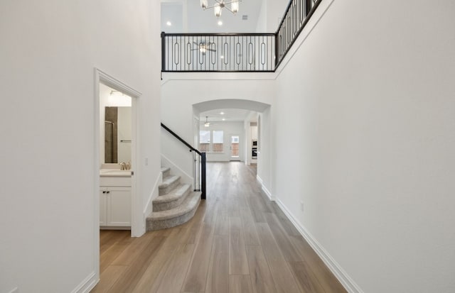 hall featuring light wood-style flooring, stairs, arched walkways, and a sink