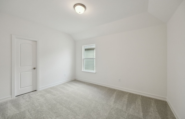 carpeted empty room featuring vaulted ceiling and baseboards