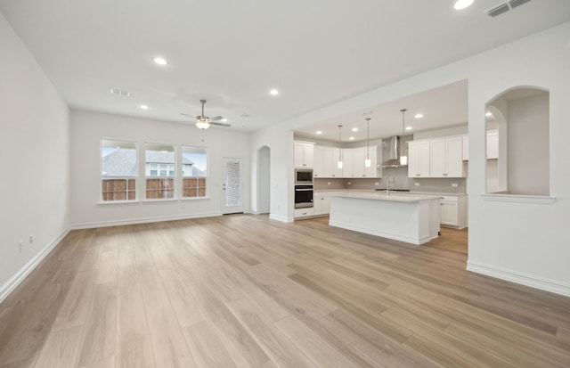 unfurnished living room with arched walkways, ceiling fan, recessed lighting, visible vents, and light wood-style floors