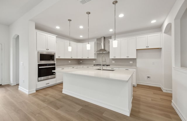 kitchen with arched walkways, wall chimney exhaust hood, appliances with stainless steel finishes, and light wood finished floors