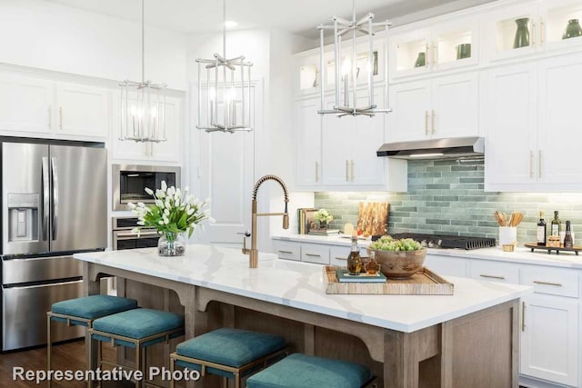 kitchen featuring white cabinetry, stainless steel refrigerator with ice dispenser, hanging light fixtures, and an island with sink