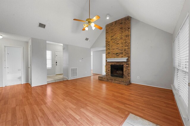 unfurnished living room featuring light wood-type flooring, high vaulted ceiling, a brick fireplace, and ceiling fan