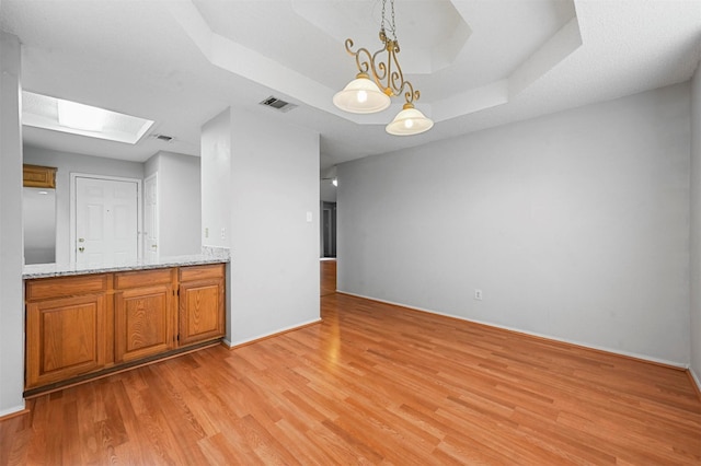 kitchen with a skylight, light stone countertops, hanging light fixtures, a tray ceiling, and light wood-type flooring