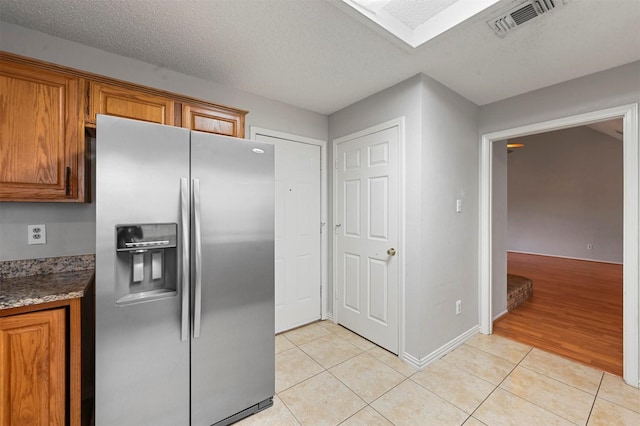 kitchen featuring a textured ceiling, light tile patterned flooring, and stainless steel refrigerator with ice dispenser