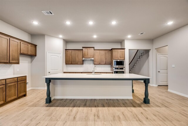 kitchen with a breakfast bar, a center island with sink, stainless steel appliances, and light hardwood / wood-style flooring