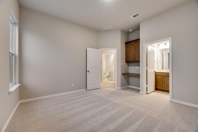 unfurnished bedroom with ensuite bathroom and light colored carpet