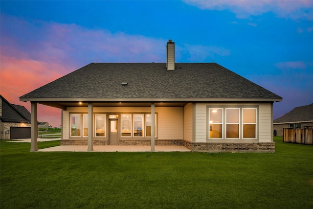 back house at dusk featuring a yard and a patio