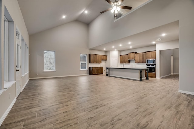 unfurnished living room featuring ceiling fan, sink, high vaulted ceiling, and light wood-type flooring