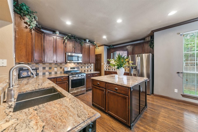 kitchen featuring light stone countertops, tasteful backsplash, stainless steel appliances, sink, and a center island