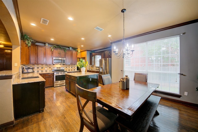 kitchen with light stone countertops, tasteful backsplash, stainless steel appliances, sink, and decorative light fixtures