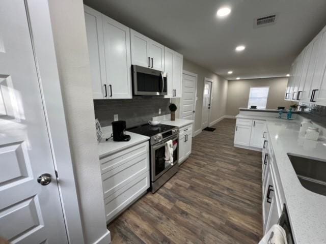 kitchen featuring decorative backsplash, white cabinetry, dark wood-type flooring, and appliances with stainless steel finishes