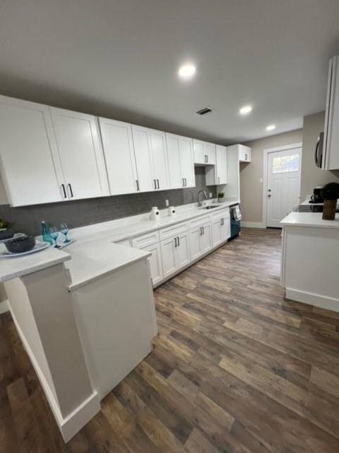 kitchen with kitchen peninsula, sink, black dishwasher, dark hardwood / wood-style floors, and white cabinetry