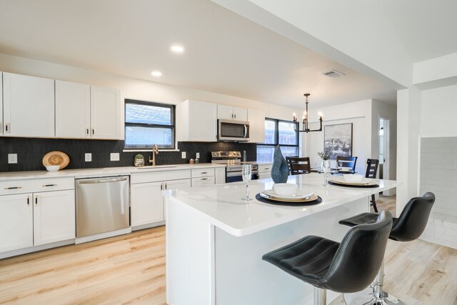 kitchen featuring decorative light fixtures, stainless steel appliances, white cabinetry, and an island with sink