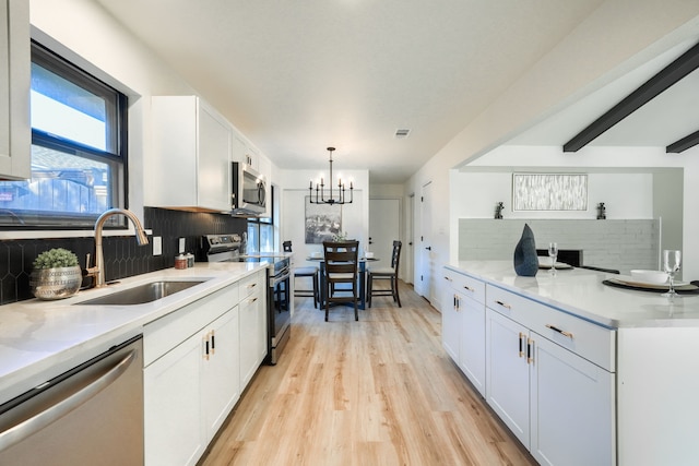 kitchen featuring appliances with stainless steel finishes, backsplash, sink, white cabinets, and hanging light fixtures