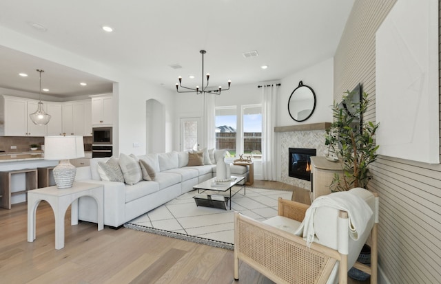 living room with an inviting chandelier, a tiled fireplace, and light hardwood / wood-style floors