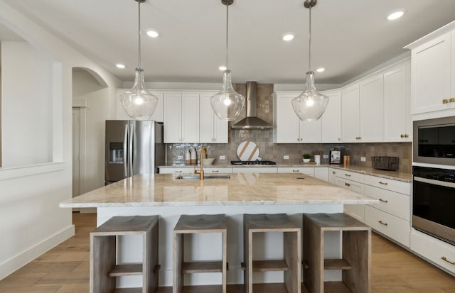 kitchen featuring an island with sink, sink, wall chimney range hood, and stainless steel fridge