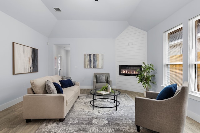 living room with a large fireplace, lofted ceiling, and light hardwood / wood-style flooring