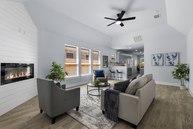 living room with wood-type flooring, a large fireplace, vaulted ceiling, and ceiling fan