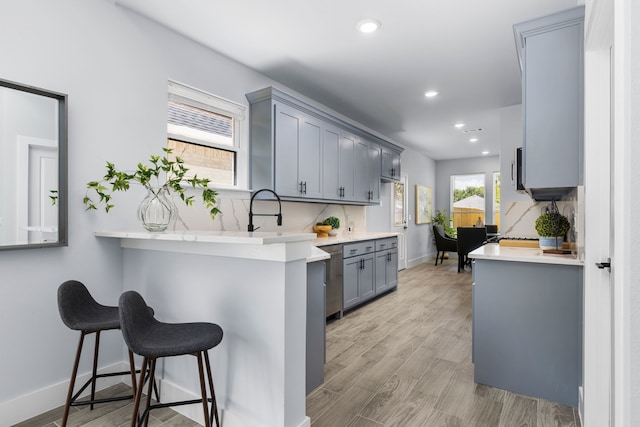 kitchen featuring gray cabinetry, a breakfast bar, dishwasher, backsplash, and kitchen peninsula